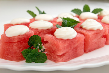 Slices of watermelon with vhipped cream scoops on top. Sweet summer dessert on white plate. Vegeterian dieting healthy eating.