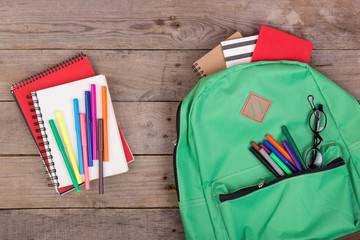 Backpack and school supplies: notepad, felt-tip pens, eyeglasses on brown wooden table