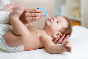 Mother or doctor cleans baby's nose with blower, while infant is lying and smiling.