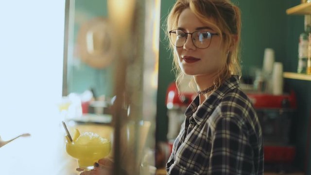 Portrait young attractive caucasian waitress standing side view barkeeper holding glass cocktail orange thoughtful smiling looking camera service bar cafe hipster barmaid woman stylish pretty nice