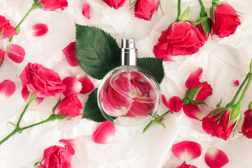 Feminine perfume bottle top view on wrapping gift paper, rose flowers, petals, leaves scattered around. 