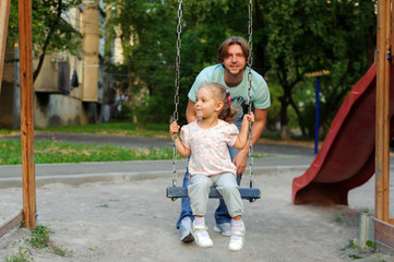 A girl with a dad on the playground on a swing