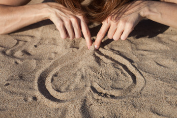 Girl drawing heart in the sand