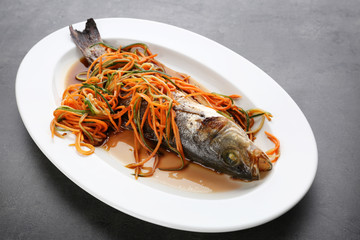 Plate with delicious fish, sauce and vegetables on table