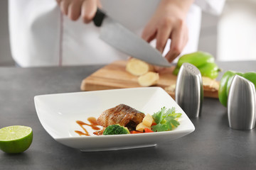 Plate with delicious fish in sauce and blurred chef on background