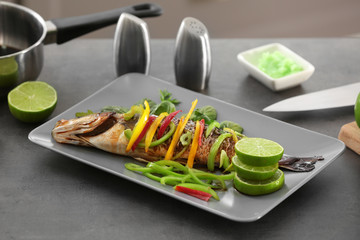 Serving plate with delicious fish in sauce and vegetables on table