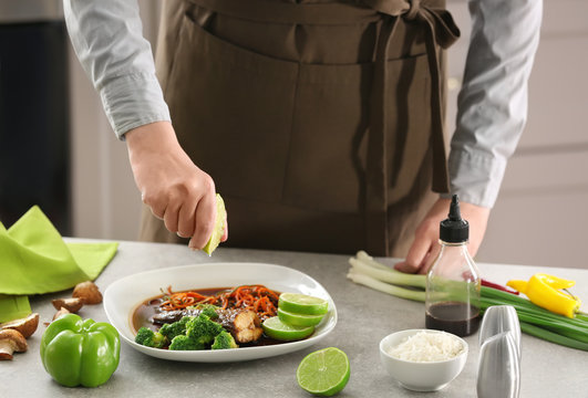 Chef squeezing lime juice onto plate with delicious fish in sauce and vegetables