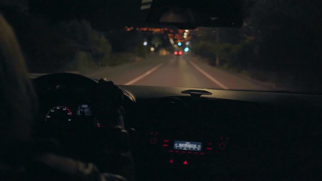 Night time shot of woman driving car through dark road with few lights, looking into side mirrors, checking situation with traffic for danger or safety, hands on steering wheel