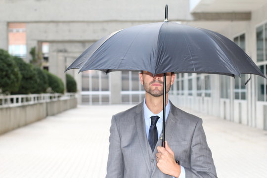 Businessman hiding under an umbrella in office space