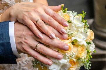 Obraz na płótnie Canvas Hands of a young couple with engagement rings on the background of a bouquet.