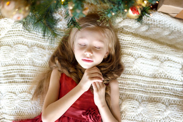 Happy girl lying under the Christmas tree and dream. The concept of the holiday, Christmas, New year. High top view.