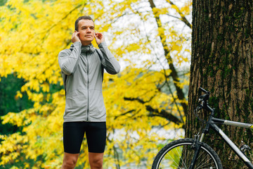 Young pretty athletic man standing with bicycle in autumn park. Fall season background. Male...