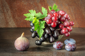 Still life with fruits: grape, fig, plum in the antique copper tin cup