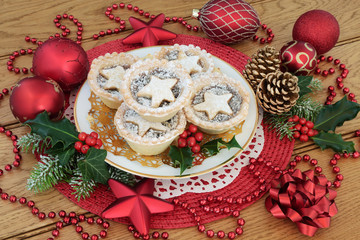 Christmas mince pies on a plate with red and gold bauble decorations, holly, ivy, pine cones and...