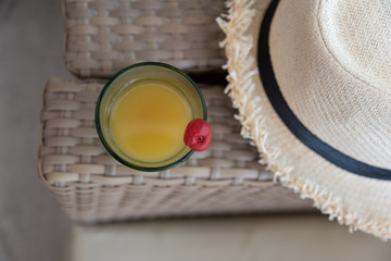 Fresh welcome drink made with passion fruit & red cherry put on chair beside casual hat
