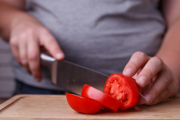 Dieting, healthy low calorie food, weight losing concept. Overweight woman slicing tomato on a chopping board. Making salad, low carb diet