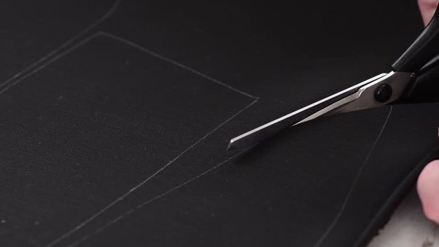 Seamstress cuts scissors along line drawn curl on black leather.