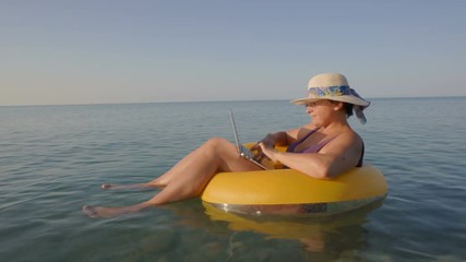 Middle aged female working on laptop computer in orange inflatable life ring on vacation