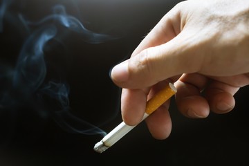 smoking Cigarettes in hand with a soft-focus background black.