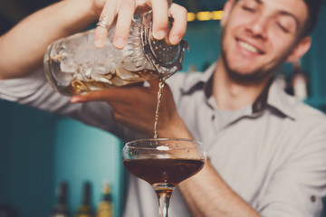 Young bartender pouring cocktail drink into glass