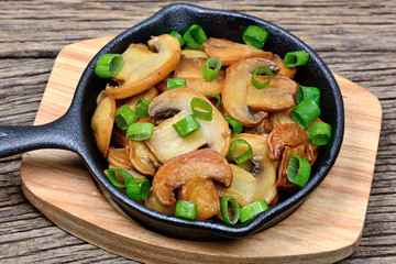 Champignon with green onion in a fry pan on bamboo support