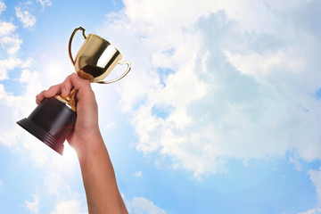 Asian boy holding a gold trophy cup for first place champion award on blue sky. Boy holding up a...