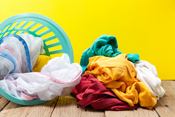 Pile of dirty laundry in washing basket on wooden,yellow background.