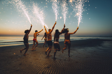 Group of friends having fun running on the beach with sparklers