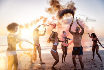 Group of friends having fun running on the beach with smoke bombs