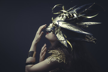 Jewelry, Girl in dress made of golden threads with golden mask, beautiful young brunette