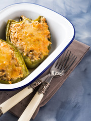 Bell peppers stuffed with mixed cereals, meat and cheese baked in enamel tin on blue