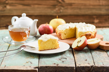 Tasty oldfashioned cake with cream icing served with tea and raw apples on shabby turquoise table