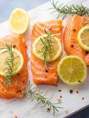 Raw salmon pieces on wooden board with herbs, salt and spices