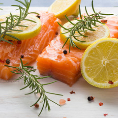 Raw salmon pieces on wooden board with herbs, salt and spices