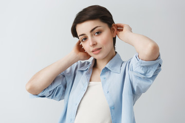 Portrait of beautiful young student girl with big brown eyes and short hair holding hair with hands , looking in camera and gently smiling.