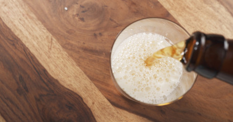 top view pouring lager beer from bottle into glass on wood table