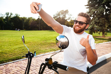 Fototapeta premium Smiling bearded man in sunglasses sitting on modern motorbike
