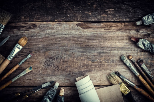Paint tubes, brushes for painting and palette knifes on old wooden background. Top view. Flat lay. Retro toned.