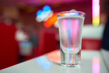 glass of iced vodka is on the table in the club on red interior