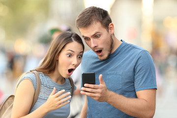 Amazed couple watching on line media in a phone
