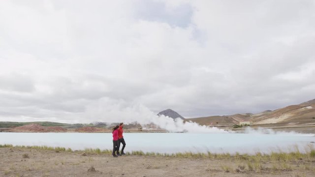 Iceland travel people by geothermal energy power plant and hot spring in Namafjall in Lake Myvatn area. Couple on travel in Icelandic nature landscape. SLOW MOTION 60 FPS RED EPIC.