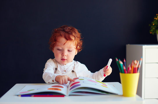 cute redhead baby boy drawing in developing book at the desk