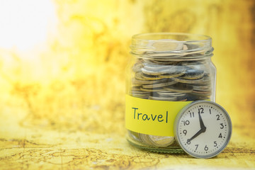 Time, Travel and Saving Concept. Full of coins in clear bottle with yellow label note with Travel word and vintage round watch on wolrd map.