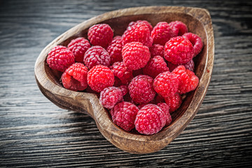 Heart-shaped bowl with ripe raspberries on wooden board