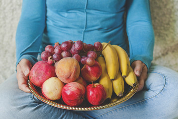 Female hands hold a dish of fruit, fruit mix, bananas, pomegranates, apples and peaches. View from...