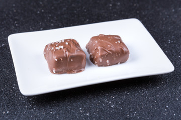 Two salted chocolate caramels on a black background