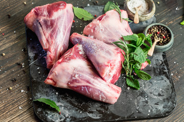 Raw lamb shanks with salt and pepper on stone tray on rustic wooden table, selective focus © jarvna