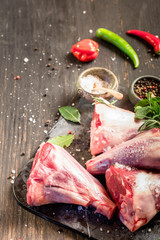 Raw lamb shanks with salt and pepper on stone tray on rustic wooden table, selective focus