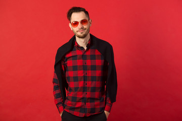 portrait of a stylish young guy in a checkered shirt and wearing red glasses on a red background