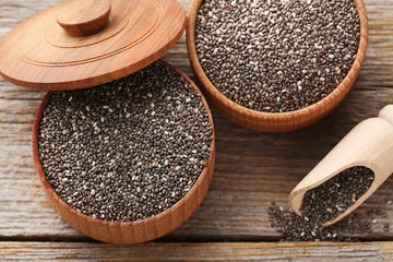 Heap of chia seeds in bowls and scoop on grey wooden table